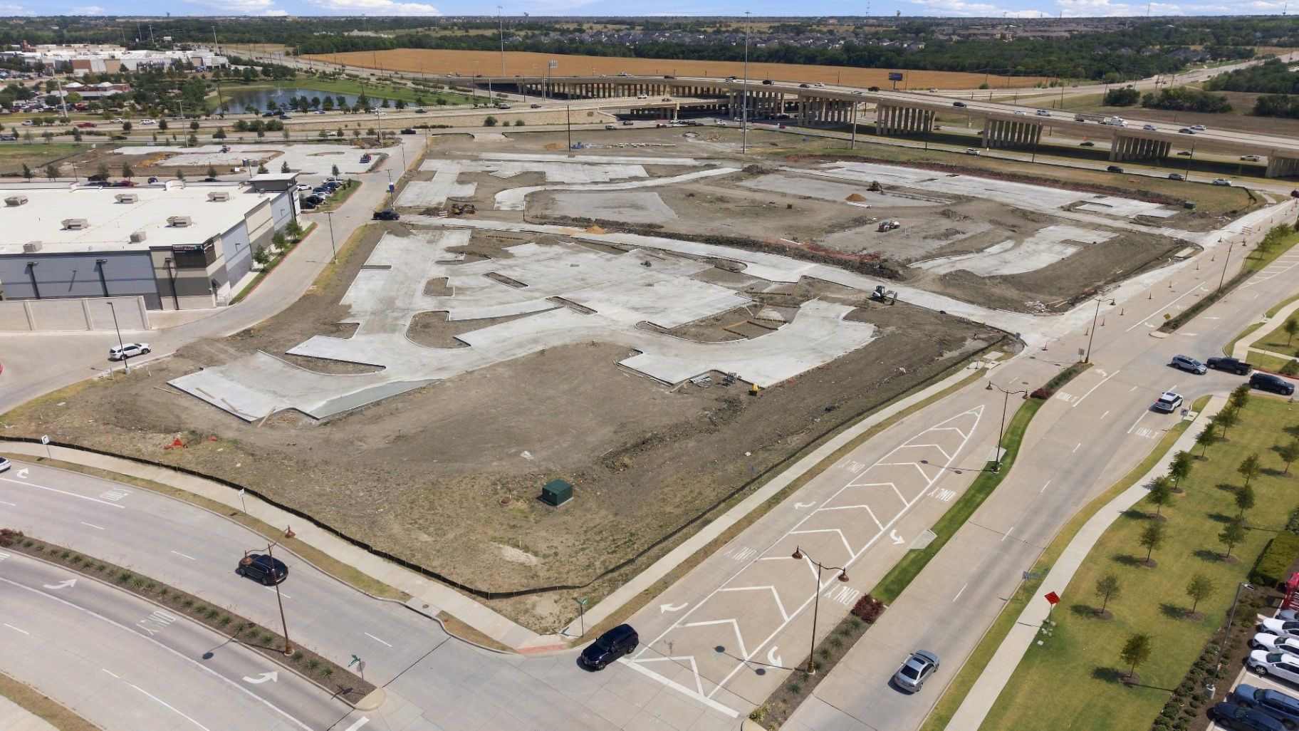 Active commercial construction site with structural steel, cranes, equipment, and surrounding roads.